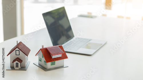 2 wooden house designs on wooden table with laptop, preparation ideas for buying a house model and real estate economy.