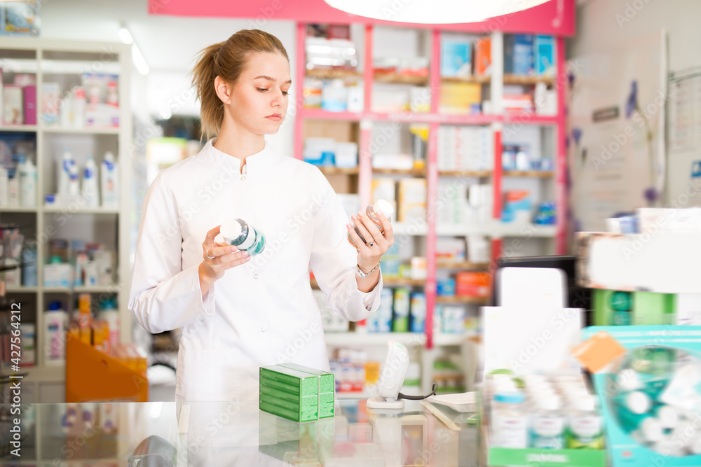 Smiling female druggist in white coat working in pharmacy