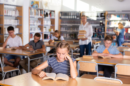 Group of teenage students reading books in college library