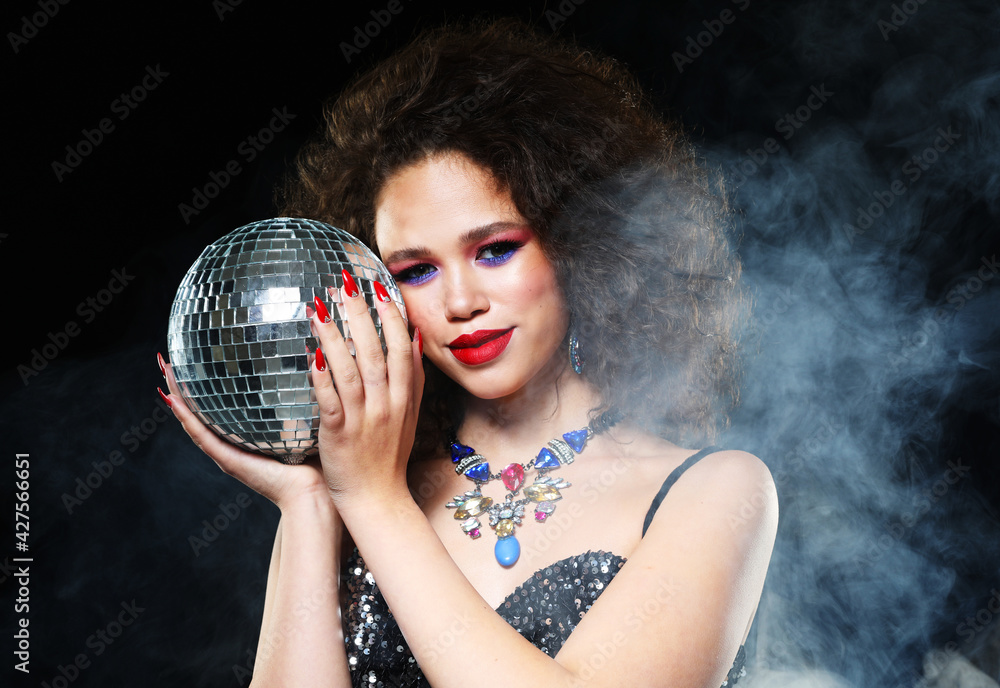 Naklejka premium Close up portrait of young african woman with bright make up holding disco balls over dark background