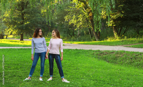 Mom and her adult daughter hold hands in a summer park, happy women