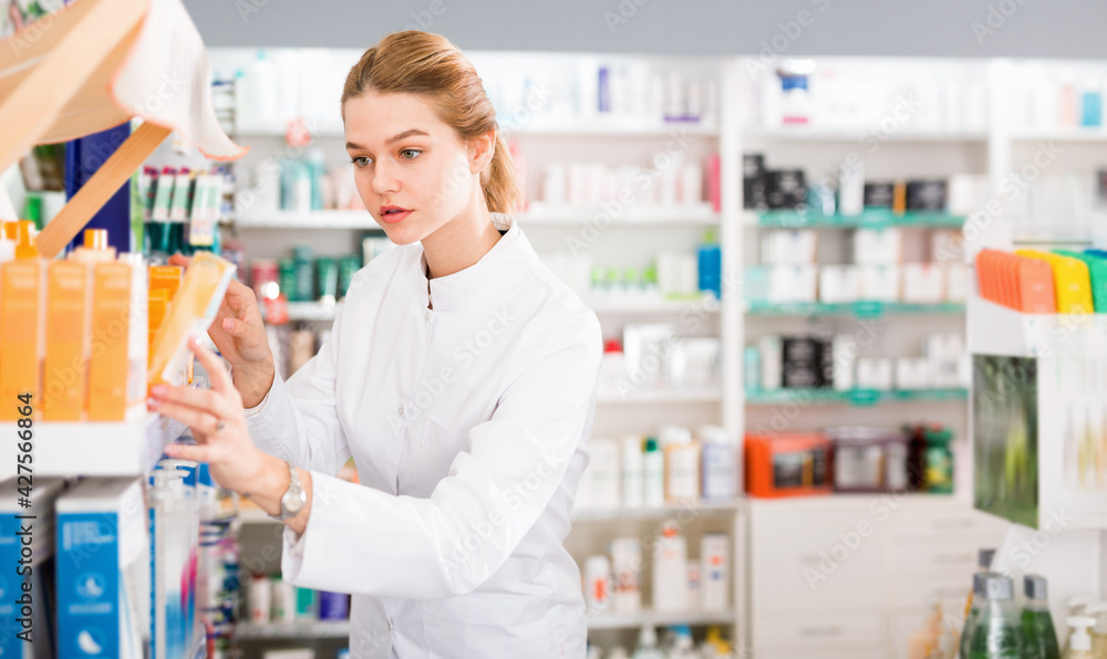 Cheerful positive female pharmacist searching for reliable body care products in pharmacy