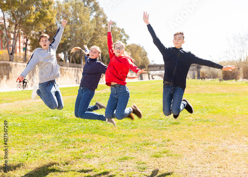 Four joyful teens jump on a spring lawn