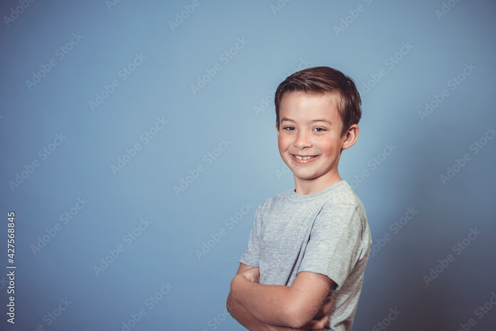 cool, young boy with grey t-shirt is posing in front of blue background in the studio cool, young boy with grey t-shirt is posing in front of blue background in the studio