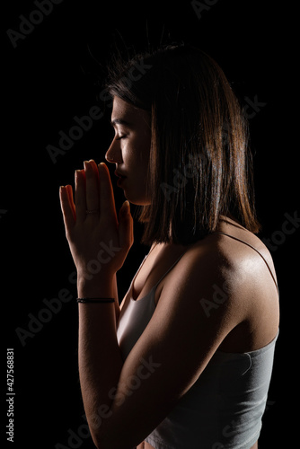Portrait of woman praying isolated on black background. Vertical shot.