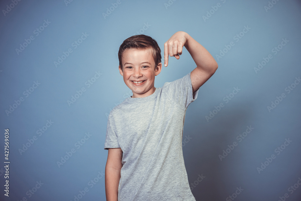 Obraz premium cool, young boy with grey t-shirt is posing in front of blue background in the studio