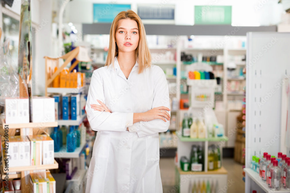 Portrait of young pleasant smiling cheerful positive female pharmacist in modern drugstore