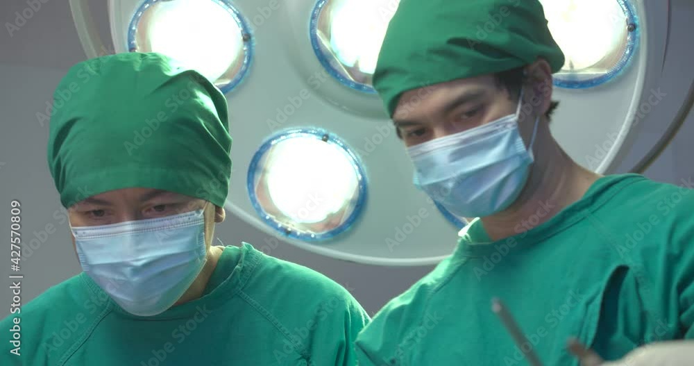 Team of asian doctors wearing full surgical scrubs performing operation on a patient in operating theater at the hospital. Teamwork, Healthcare and medical technology concept. Team of asian doctors wearing full surgical scrubs performing operation on a patient in operating theater at the hospital. Teamwork, Healthcare and medical technology concept.