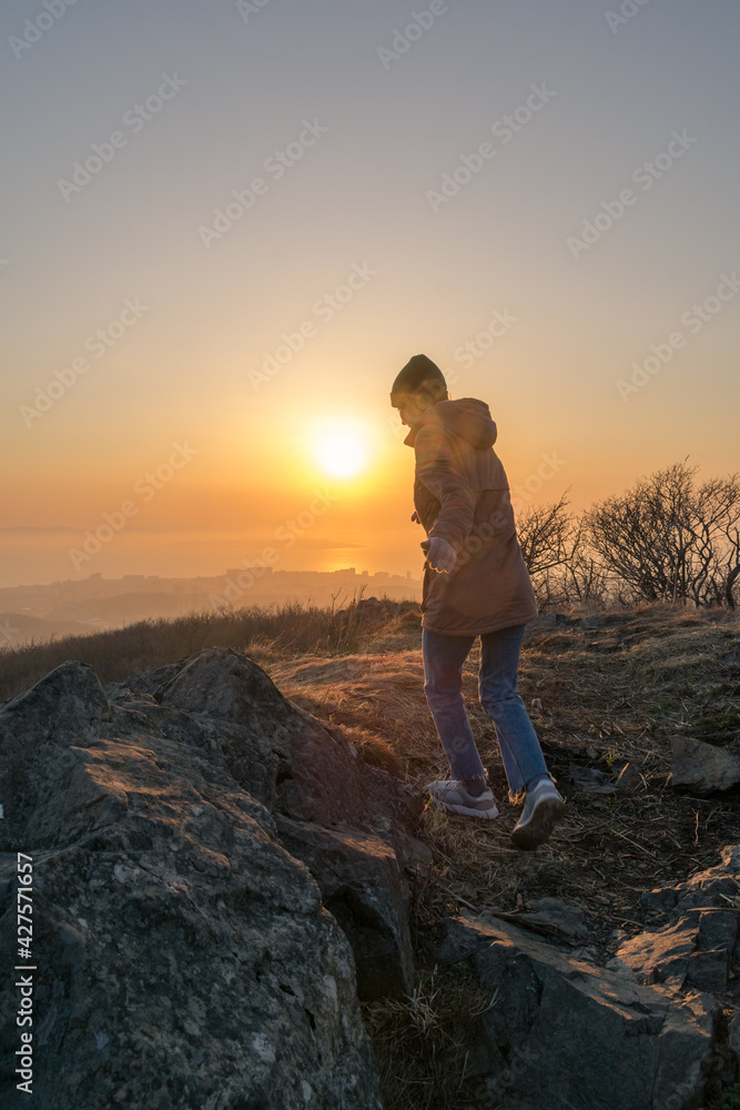 Girl in a jacket and a hat on the mountain during sunset