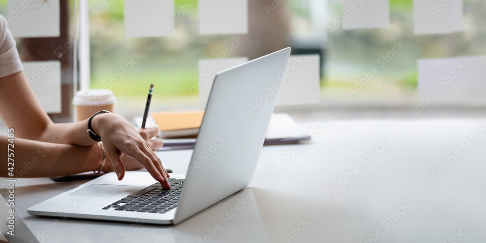 Cropped photo hand of woman writing making list taking notes in notepad working or learning online with laptop at home Cropped photo hand of woman writing making list taking notes in notepad working or learning online with laptop at home