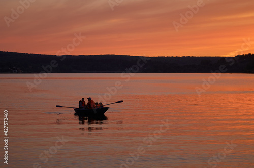 Rowboat with unrecognizable persons on water at sunset