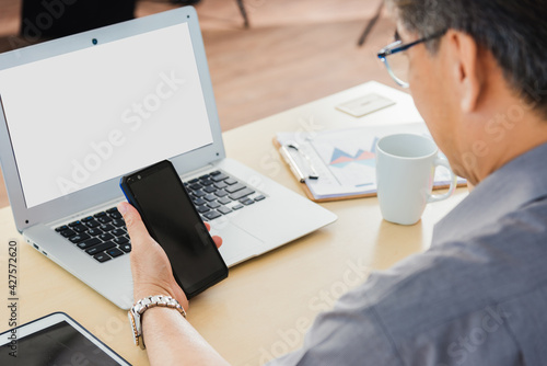 Old businessman using the mobile phone to video call conference on desk table at office. Asian senior business man working online on modern smartphone he looking at screen for remote online studying