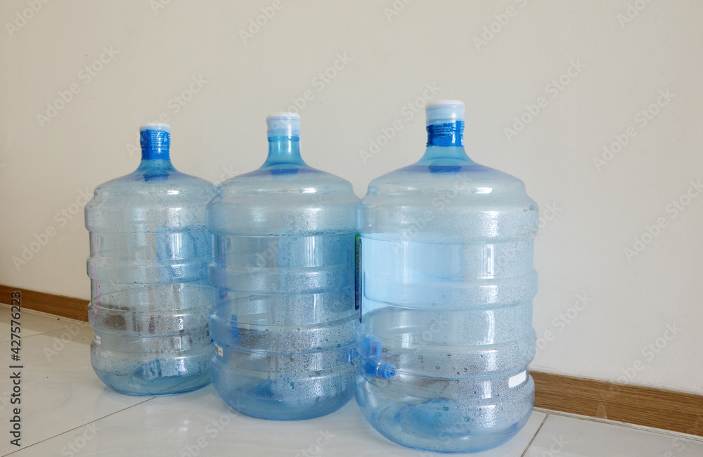 Empty used plastic water cooler bottles line up on the floor Empty used plastic water cooler bottles line up on the floor