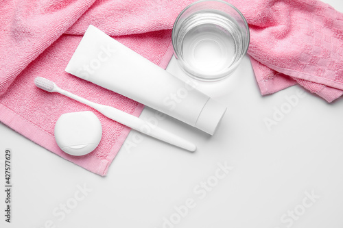 Tooth brush with paste, floss, glass of water and towel on white background