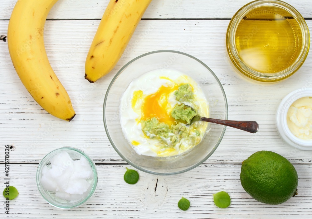 Natural ingredients for smoothing, softening and hydrating hair. Banana, avocado, lime, yogurt, shea butter, egg yolk, coconut and olive oil for hair mask, flat lay.