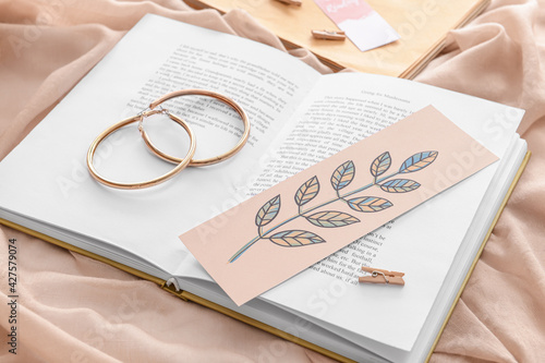 Book with bookmark and earrings on color background