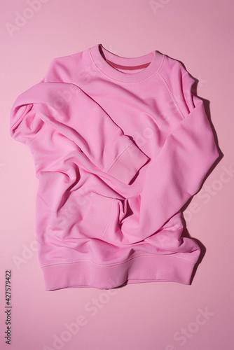 Top view of pale pink pastel sport blank sweatshirt lying vertically isolated on light pink background