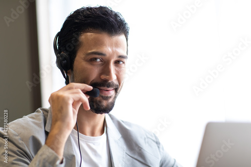 Attractive business man in suits and headsets smiling while working on desktop computer at modern office desk . Customer service assistant working in office. VOIP Helpdesk headset