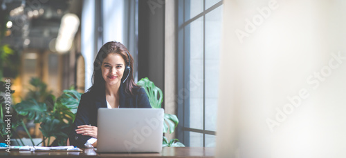 Attractive business woman Asian in suits and headsets are smiling while working with computer at office. Customer service assistant working in office. VOIP Helpdesk headset