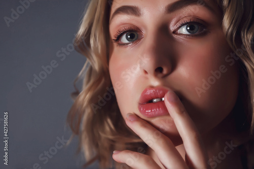 Close-up young pretty blonde woman with finger at lips flirts look against dark blue insulation background. Female emotion happy and actress of master. Concept of satisfaction inspiration. Copy space