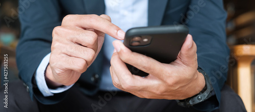young Businessman in suit holding and using smartphone for sms messages, man typing touchscreen mobile phone in office or cafe. business, lifestyle, technology and Social media network concept