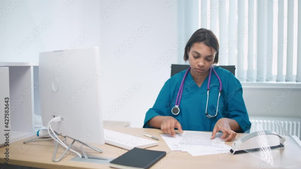 Serious female doctor sits at workplace in modern hospital and works with patients survey documents. Serious female doctor sits at workplace in modern hospital and works with patients survey documents.