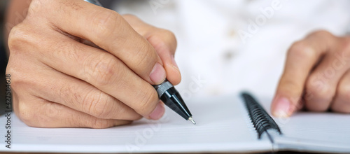 Businesswoman writing something on notebook in office or cafe, hand of woman holding pen with signature on paper report. business concepts