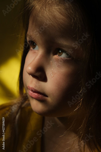 Dramatic portrait of sad little child girl with tear on the cheek and shadow on face. lonely in dark. Childhood and problems of parents and children concept.