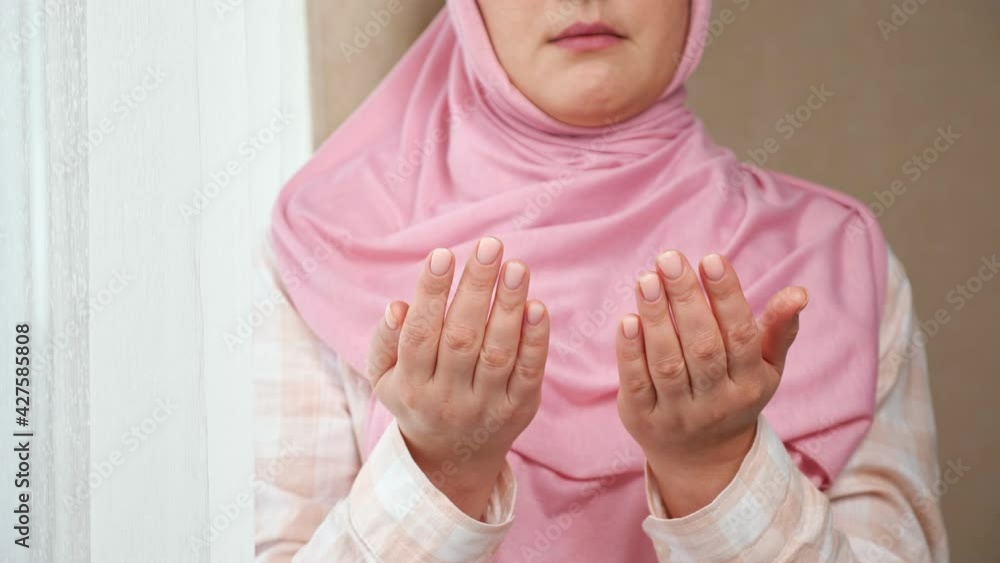 Unrecognizable woman in pink hijab reads a prayer while holding hands in front of her. Unrecognizable woman in pink hijab reads a prayer while holding hands in front of her.