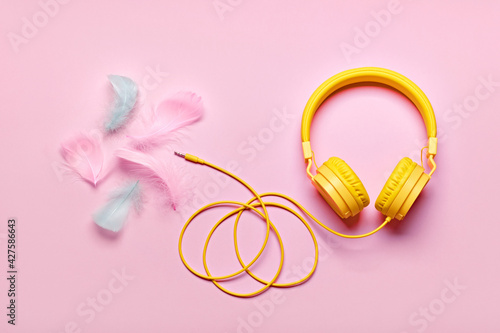 Yellow headphones and soft feathers on pink background. ASMR Stress-relieving sounds concept, flat lay © colnihko
