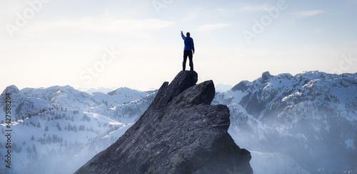 Composite. Adventurous Man Hiker on top of a Steep Rocky Cliff. over the Puffy Clouds. Sunset or Sunrise. Landscape Taken from British Columbia, Canada. Concept: Adventure, Explore, Hike, Lifestyle