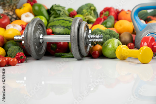 Fitness concept. Healthy nutrition: fruits and vegetables. Equipment for fitness exercises: weighing machine and dumbells. White background.