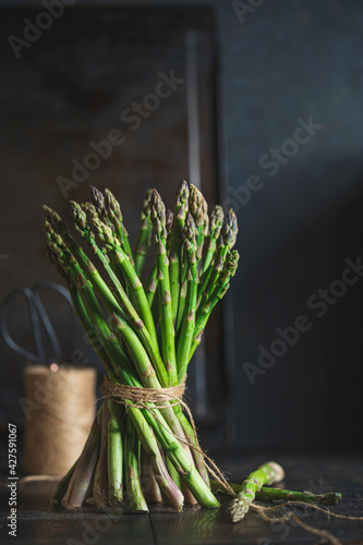 Fresh stems of green asparagus with spices around - salt crystals   dark wooden background. Macro view  copy space. Vegan  healthy eating  dieting concept. Organic vegetables.