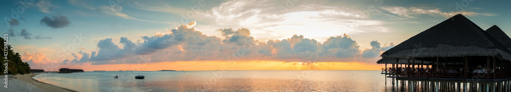 Sunset on Maldives island, luxury water villas resort and wooden pier. Beautiful sky and clouds and beach background for summer vacation holiday and travel concept. Panoramic view 
