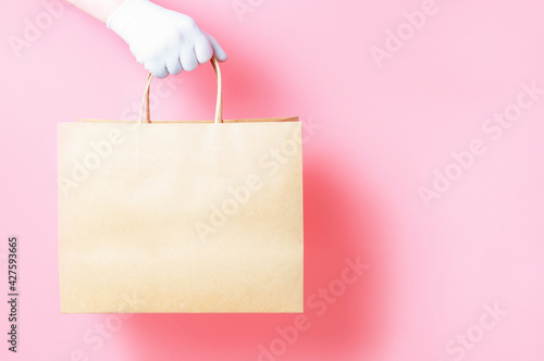 Hand in glove holds cardboard bag on pink background, food delivery concept.