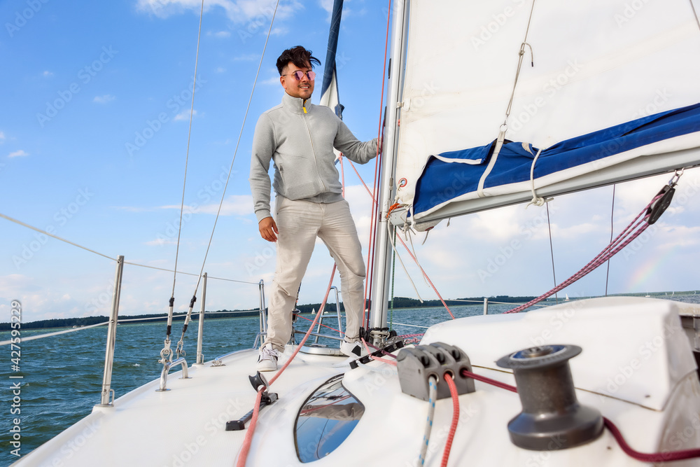 young man standing on a sailboat. Summer vacations, cruise, recreation, sport, regatta, leisure activity, service, tourism