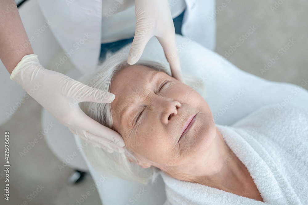 Gray-haired mature woman having a face massage and looking relaxed