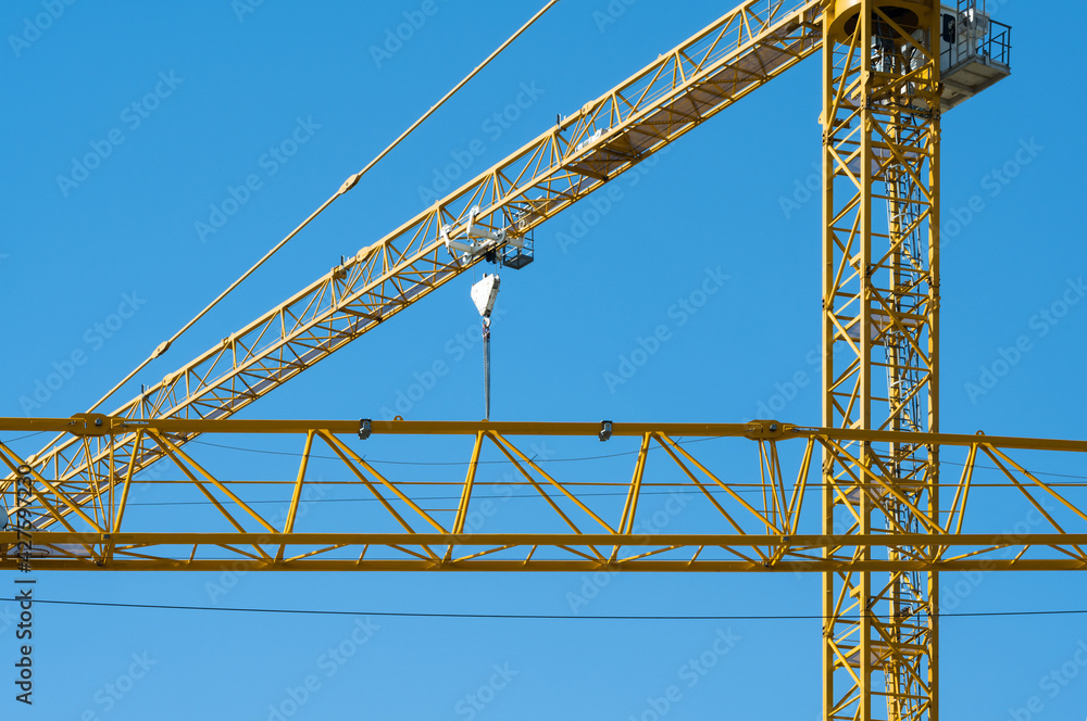A yellow construction crane made of steel pipes against a blue sky. A yellow construction crane made of steel pipes against a blue sky.