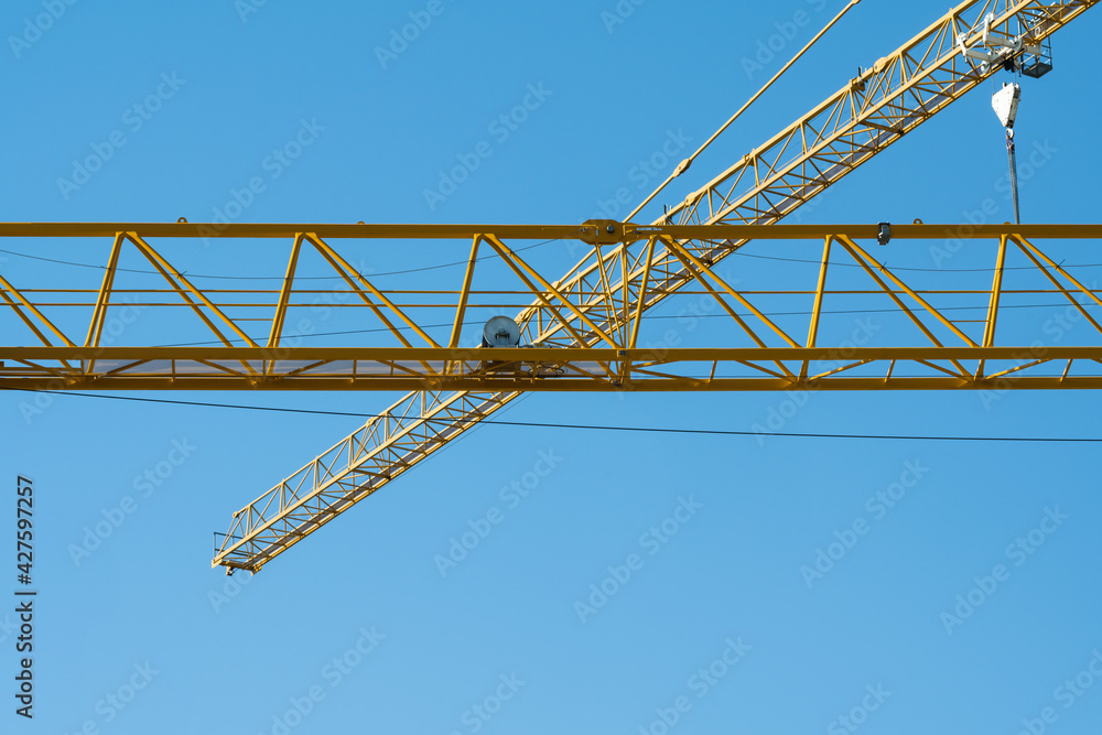 A yellow construction crane made of steel pipes against a blue sky.