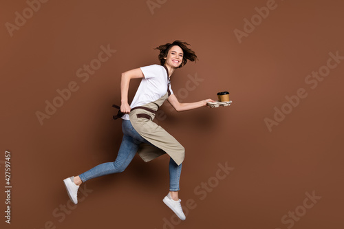 Full length body size view of attractive cheerful girl bringing coffee jumping fast service isolated over brown color background