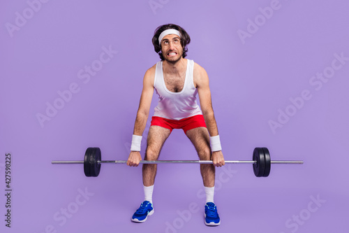 Full size photo of young crazy man in glasses look copyspace trying to lift heave barbell isolated on violet color background photo