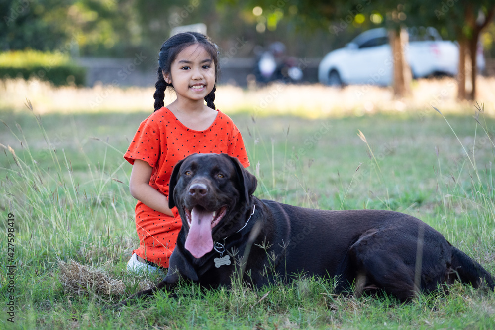 A young girl in red outfits plays with her big black dog in the backyard in the evening with her family A young girl in red outfits plays with her big black dog in the backyard in the evening with her family