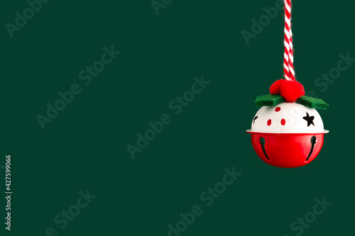 Classic Christmas bell close-up on a green background. Christmas backdrop with place for text. Red and white jingle bell photo