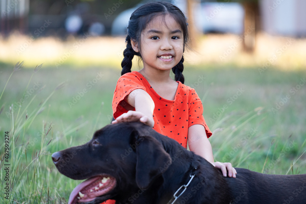 A young girl in red outfits plays with her big black dog in the backyard in the evening with her family A young girl in red outfits plays with her big black dog in the backyard in the evening with her family
