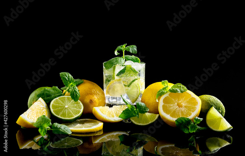Citrus lemonade with lemon, lime and ice in a glass on a black background. Splash.
