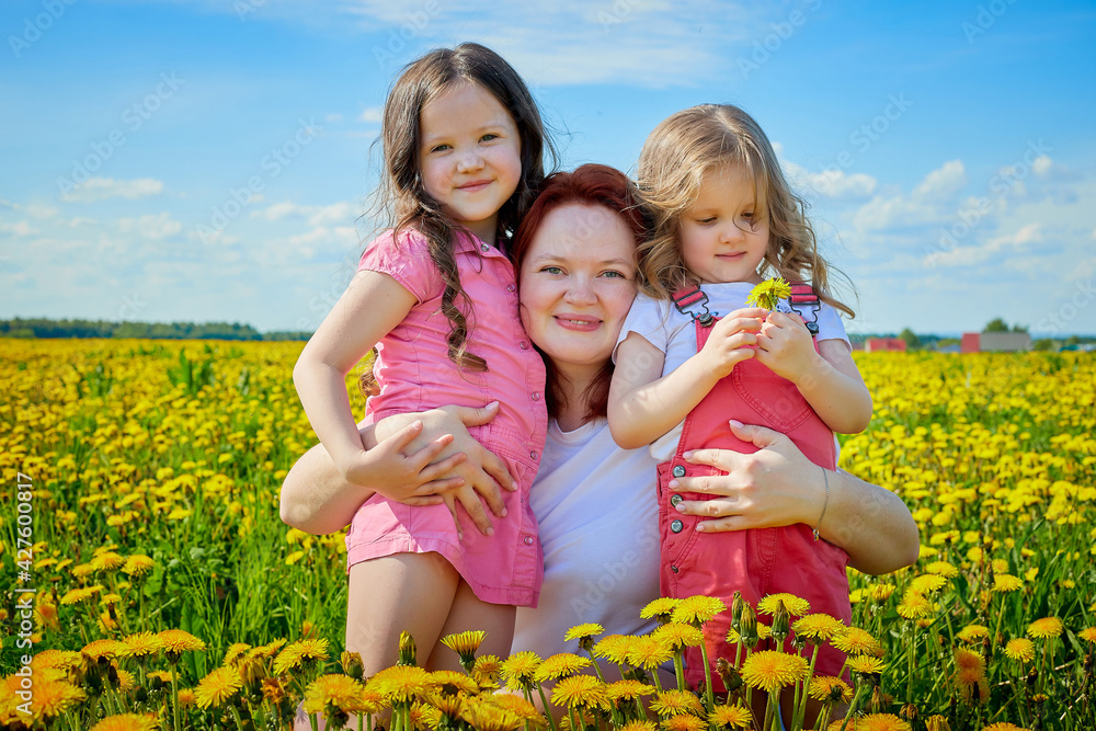 Mother and two daughters in a field with yellow dandelions. family walks in the spring in nature Mother and two daughters in a field with yellow dandelions. family walks in the spring in nature