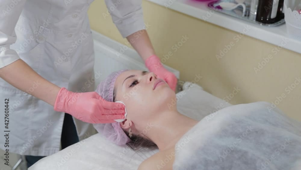 Cosmetologist's hands wiping eyebrows using cotton pads. Beautician rubs client's eyebrows with a cotton pad. Beautician in gloves is doing permanent makeup to girl. Eyebrow correction. Cosmetologist's hands wiping eyebrows using cotton pads. Beautician rubs client's eyebrows with a cotton pad. Beautician in gloves is doing permanent makeup to girl. Eyebrow correction.