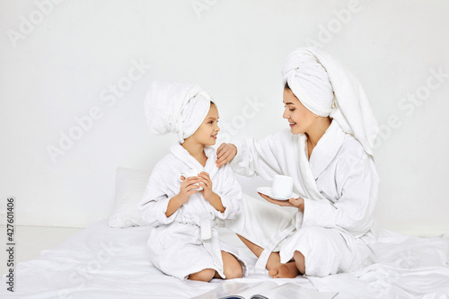 mother and daughter in white bathrobes drinking tea