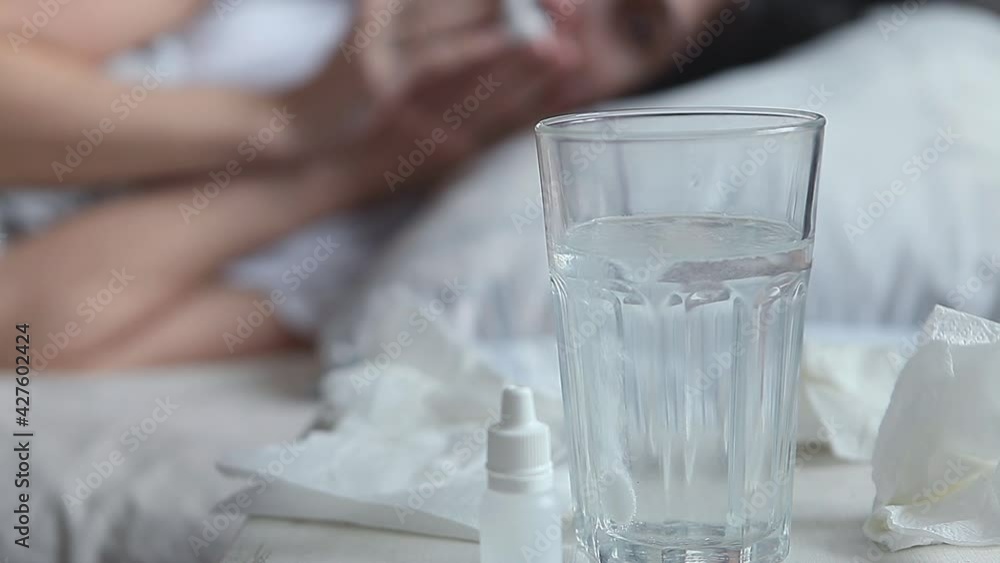 A young woman feels cold in a bed. Female hand throwing pill into a glass of water, fizzy pill dissolves in water and Drinks medicine from a glass. Fever concept. A young woman feels cold in a bed. Female hand throwing pill into a glass of water, fizzy pill dissolves in water and Drinks medicine from a glass. Fever concept.