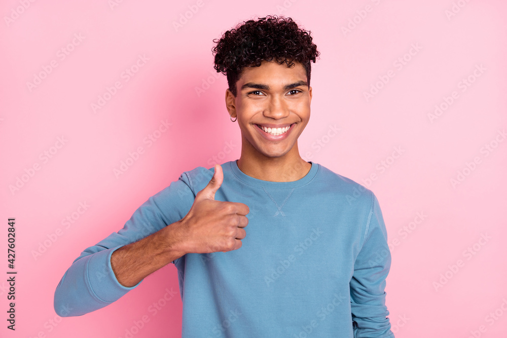 Photo of sweet cute dark skin man wear blue jumper smiling showing thumb up isolated pastel pink color background Photo of sweet cute dark skin man wear blue jumper smiling showing thumb up isolated pastel pink color background